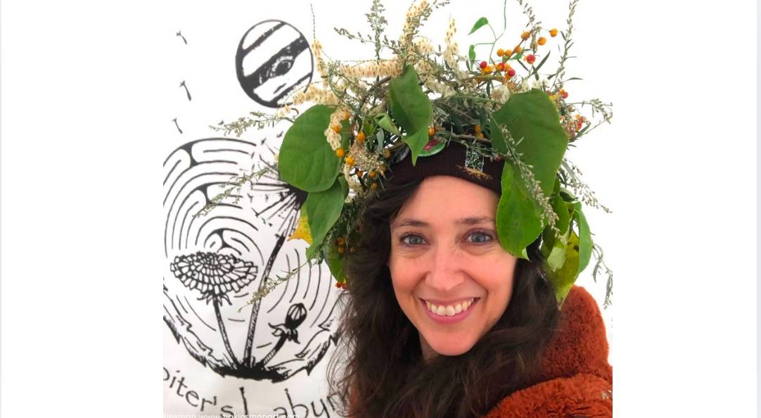 Amanda with an herbal crown in front of the Jupiter's Labyrinth Logo Sign